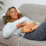 Femme allongée avec le coussin chauffant électrique sur le ventre