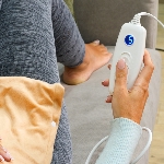 Femme allongée avec le coussin chauffant électrique sur le ventre qui utilise la commande 6 niveaux